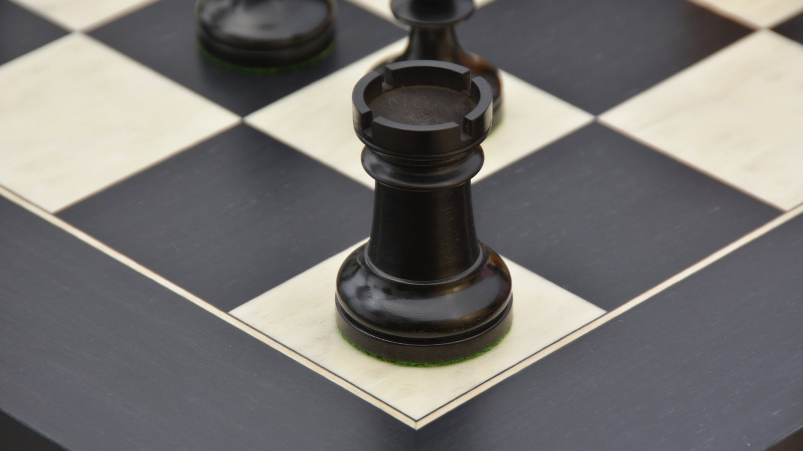 Ebonised chess pieces set up for play on the included 60cm black anigre and maple board